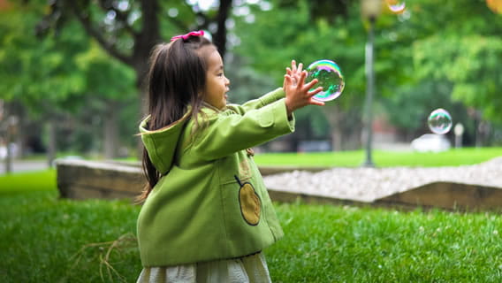 preschool girl outside reaching for bubbles