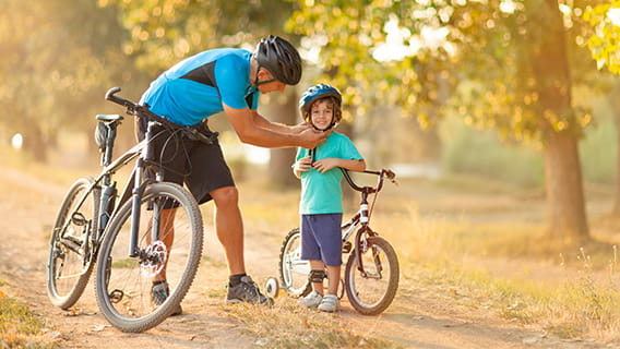 father fastening child's helmet as they stand next to their bikes