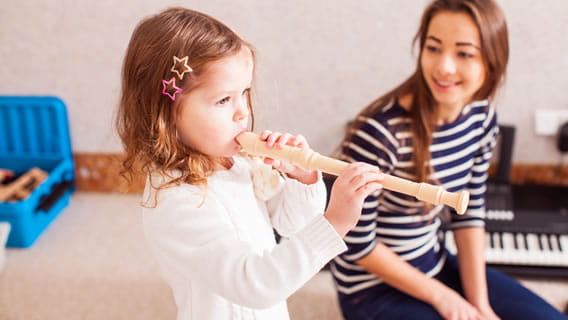 preschool girl playing recorder as mom looks on smiling