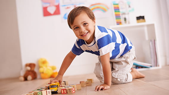 child on floor playing with blocks and school bus toy