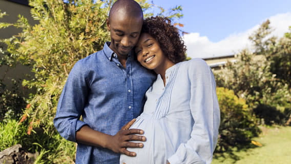 expectant, happy mom outside leaning into dad who holds belly