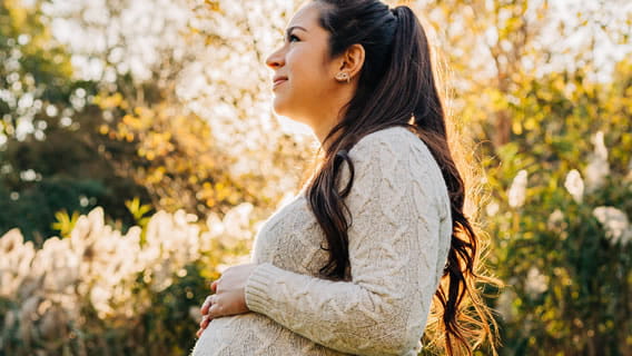 pregnant mom talking a walk outside past trees while sunny