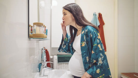 expectant mom brushing teeth in mirror in bathroom