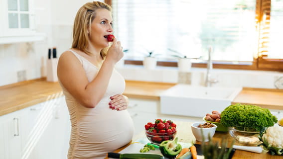 expectant mother eating strawberry in kitchen