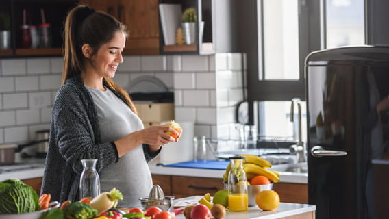 expectant mother peeling an orange at kitchen counter