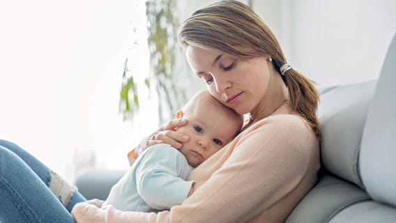 mom sitting down holding baby to chest and leaning head on baby's head