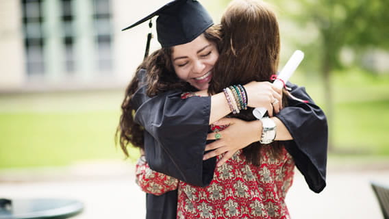 high school graduate in cap and gown hugging parent