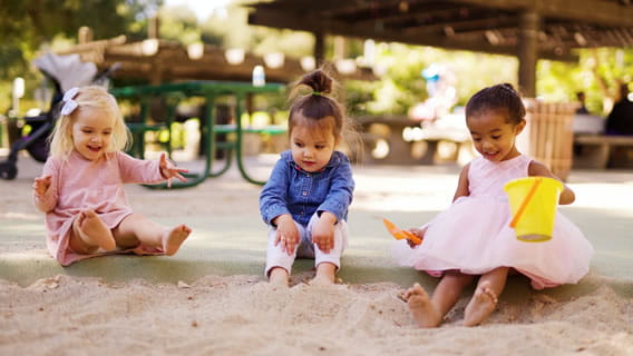 Three toddler girls outside in sandbox playing