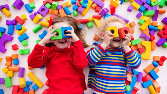 two kids lying down surrounded by blocks and holding blocks with circle openings over their eyes