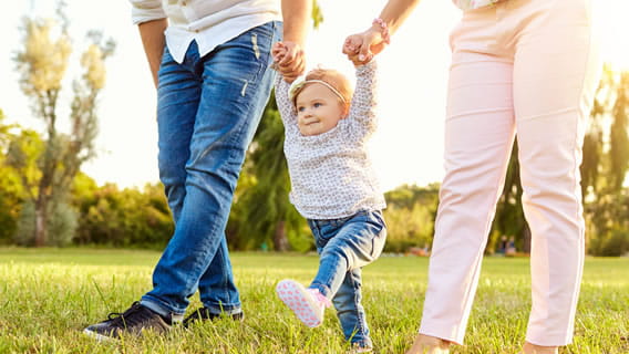 toddler walking outside with parents holding her hands