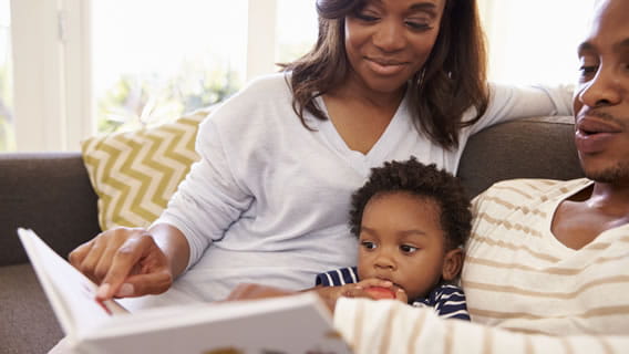 mom and dad on couch reading to toddler