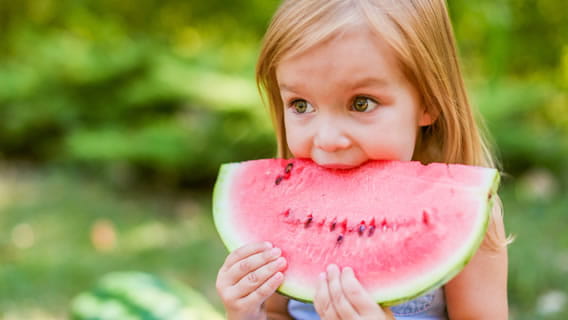 girl toddler taking a big bite out of a slice of watermelon 