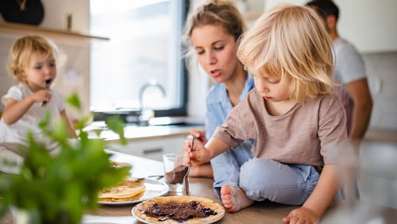 child sitting on kitchen counter eating with mother looking over shoulder