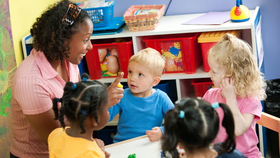 provider and four children talking at table in child care setting
