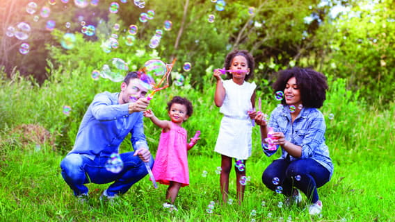 mom dad and two young girls outside playing with bubbles