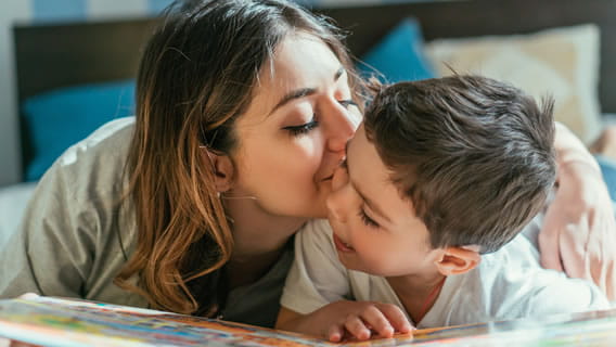 child holding a book  and mom kissing him on the cheek