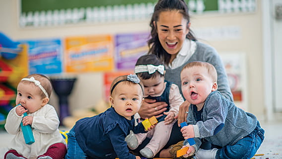 provider in care setting holding an infant with three more infants playing around her