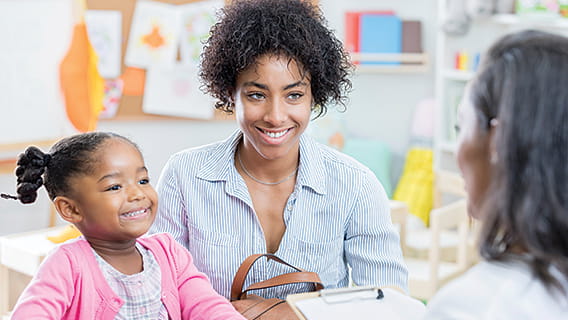 mom and daughter smiling and talking to provider who is holding a clipboard