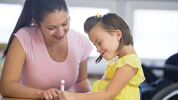 young girl drawing with marker as smiling mother looks over her