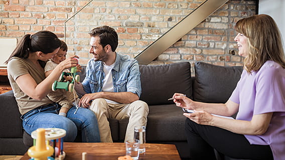 mom dad and baby on couch while nurse sits on couch across from them 