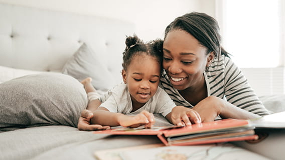 mom and infant lying on bed smiling and reading a book