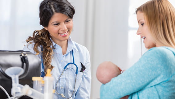doctor smiling at infant in mother's arms and mother speaks to her