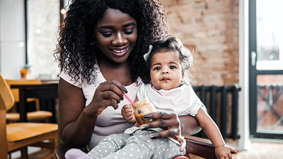 mom holding infant and smiling while feeding her baby food