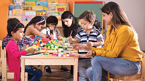 two preschool teachers at table with four preschoolers painting