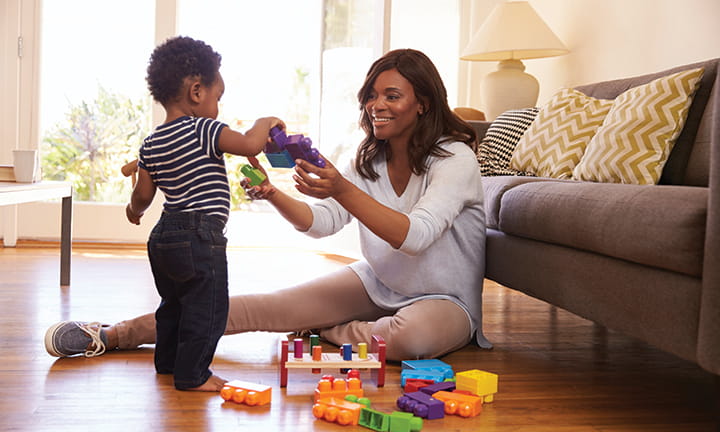 mom holding extra large lego style toy while toddler adds another on top