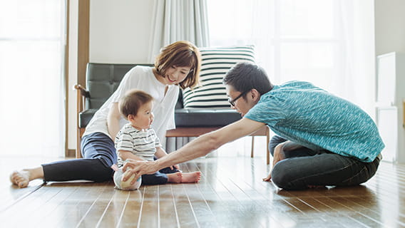 dad reaching out to toddler as mom sits behind toddler watching