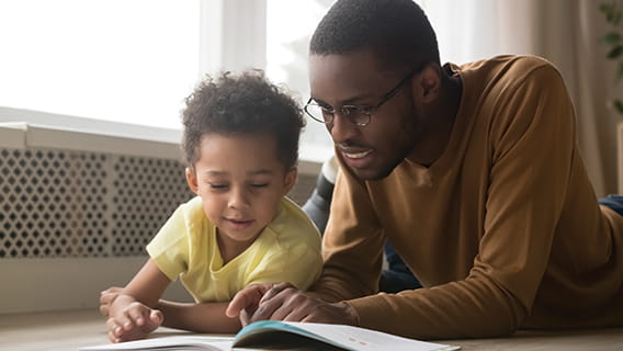 dad and toddler child lying on the floor reading a book