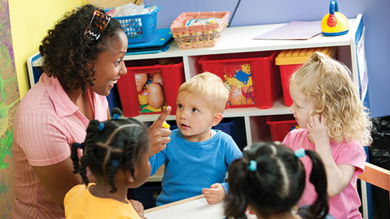 provider at a table talking to four toddlers in a care setting