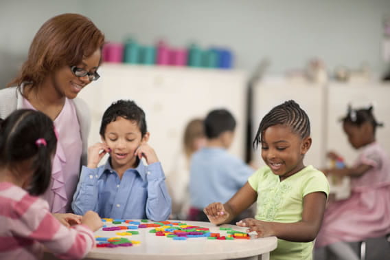 teacher at a table with three young children playing with blocks