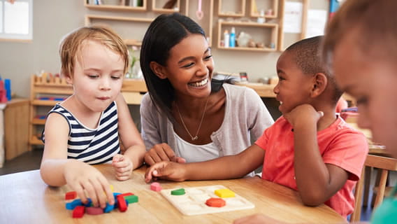 provider in care setting at table interacting with three preschool aged children