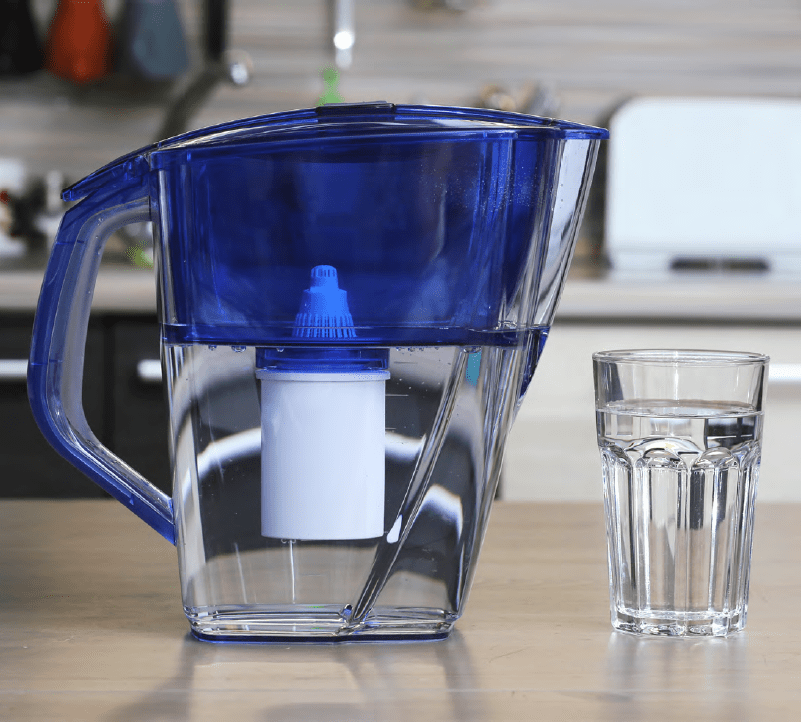 Water pitcher with a built-in filter and a glass of drinking water sitting on a kitchen countertop