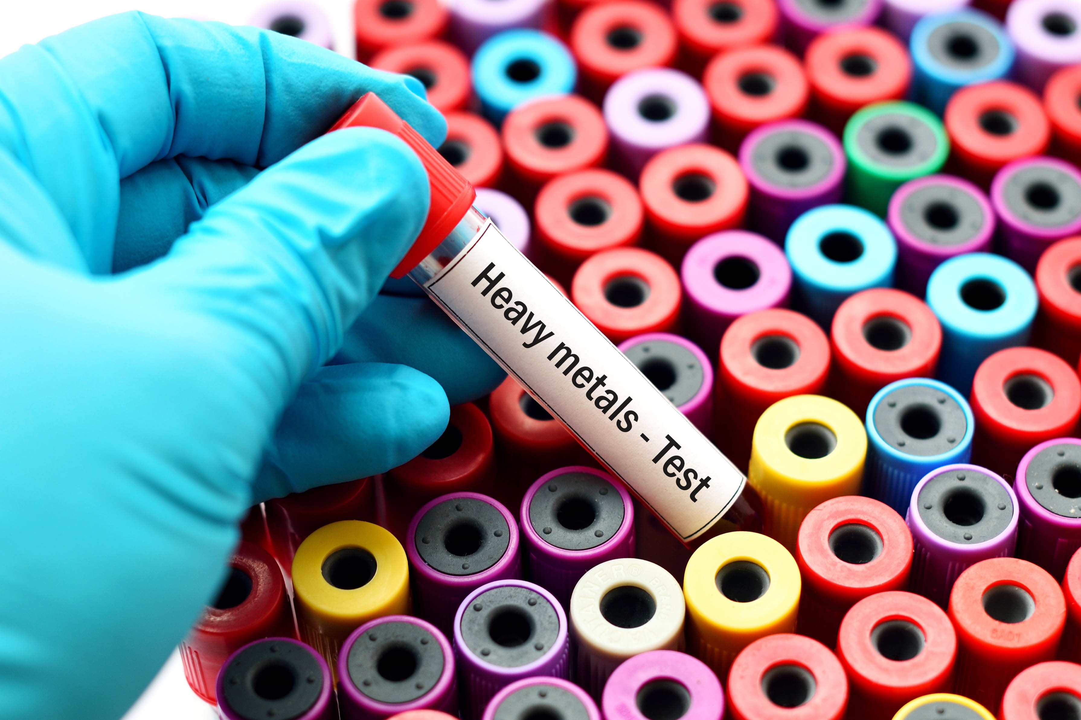Test tubes of different colors with lab technician's hand holding one tube that says "heavy metals - test." 