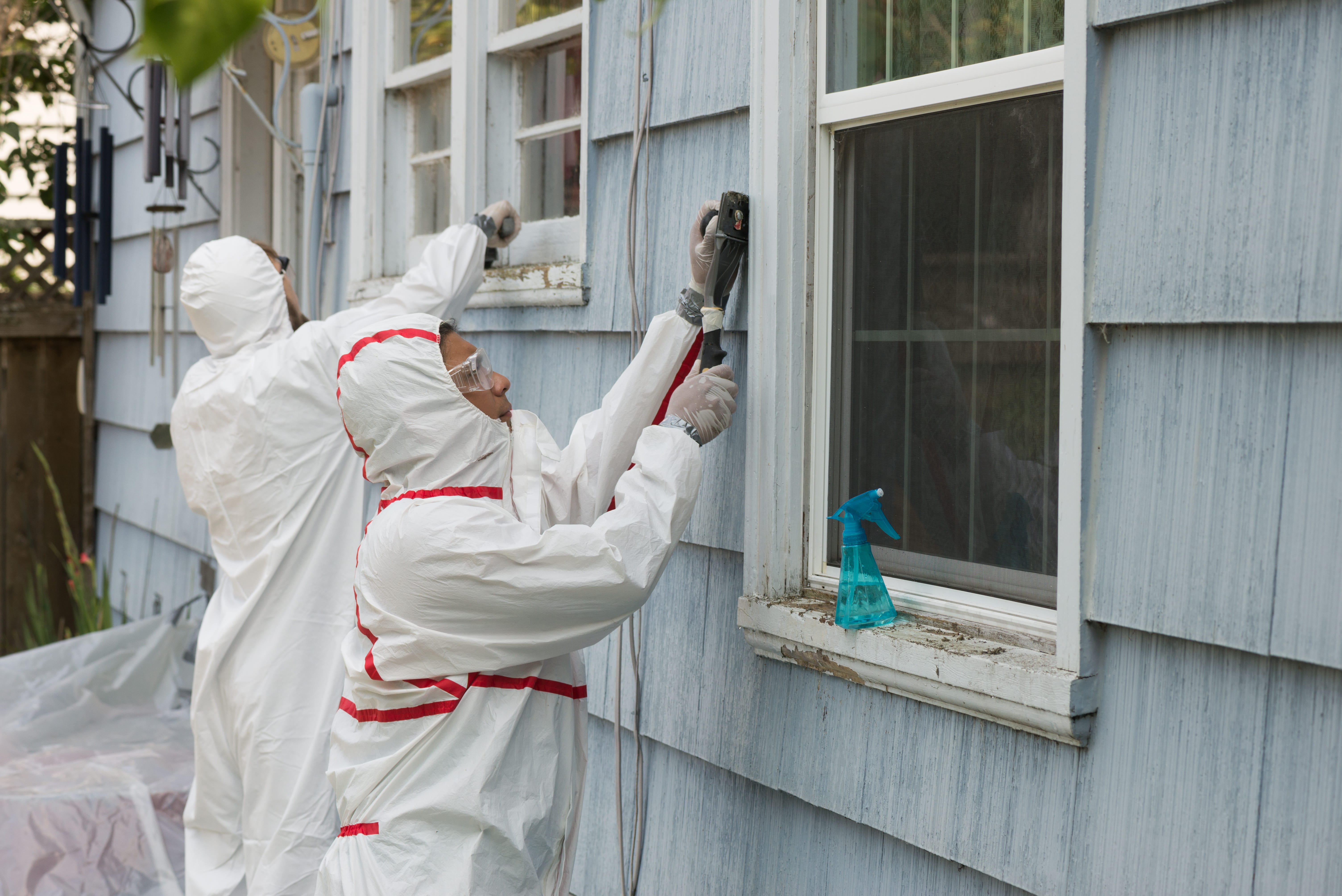 Lead abatement workers removing lead-based paint from the exterior siding of a home