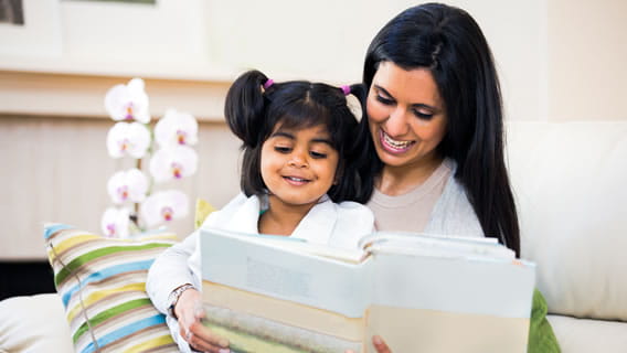 daughter sitting on mother's lap as mother reads to her