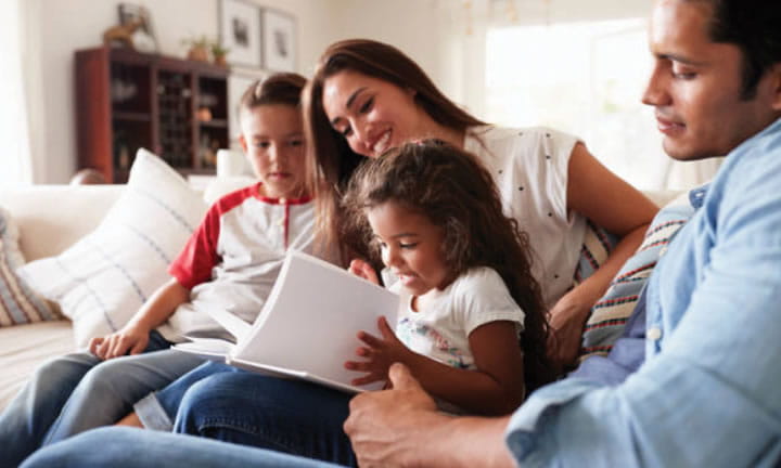 Mother and father sitting on couch reading to two young children