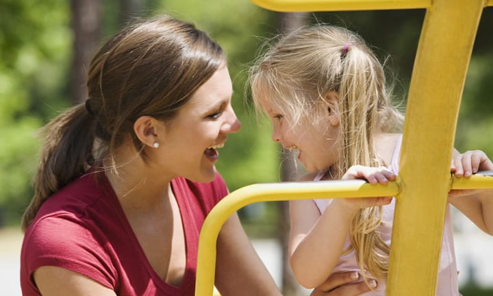 mom and young child outside smiling as child plays on jungle gym