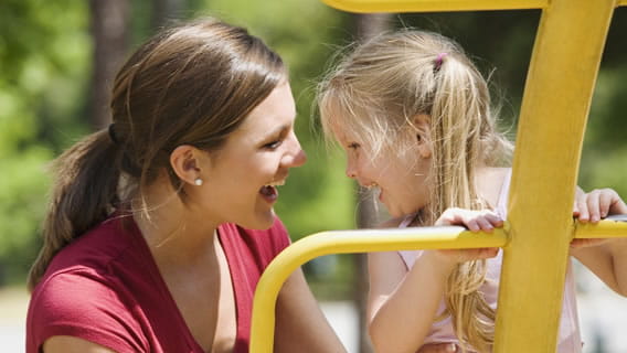 mom and young child outside smiling as child plays on jungle gym