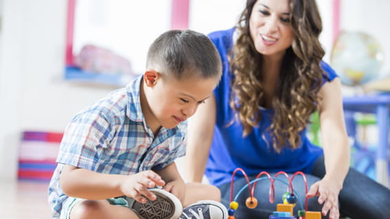 preschooler sitting on floor playing with toy as teacher encourages him