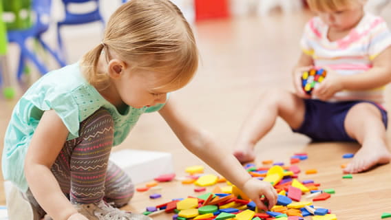 preschool taking a block from a pile while another preschooler plays with Rubik's cube