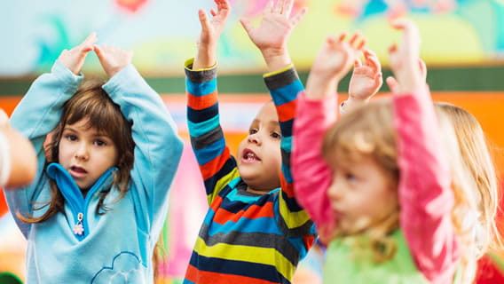 three preschoolers in classroom raising hands and singing