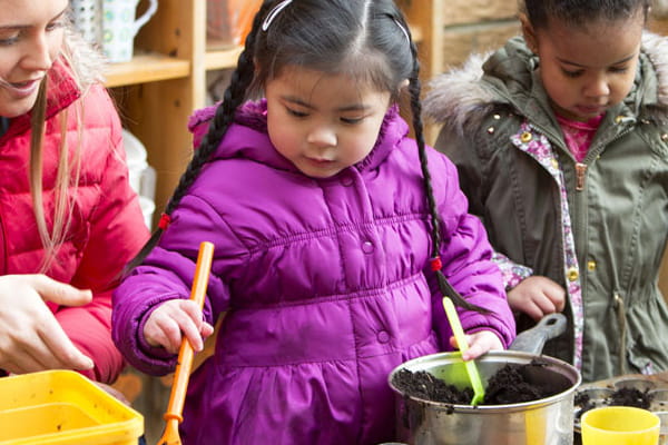 Two students with their teachers playing with soil. 