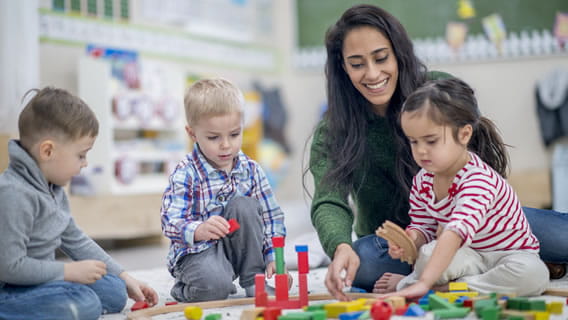 Three preschoolers and teacher sitting on the floor playing with blocks