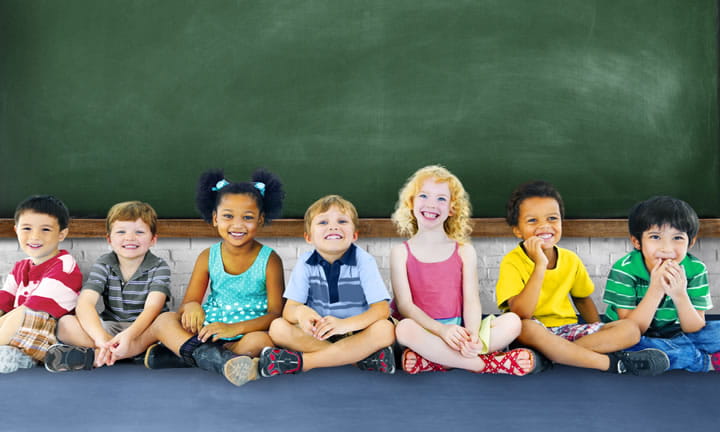 seven young children sitting on the floor in front of a chalk board and smiling