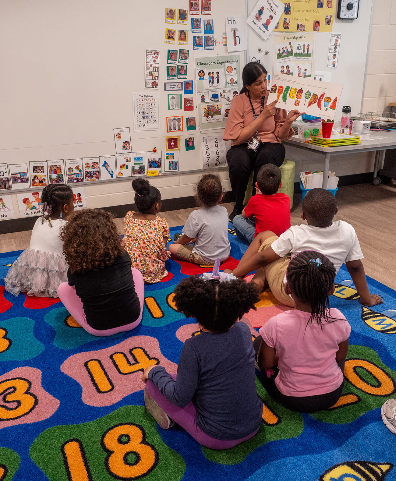Children sitting on a rug facing a teacher in a chair in a preschool classroom