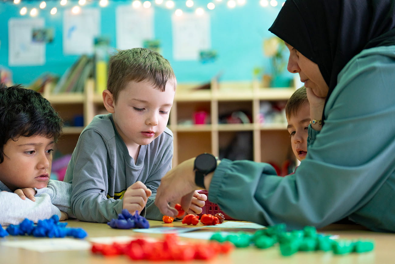 Two young children and a teacher at a table engaged in an activity in a preschool classroom setting