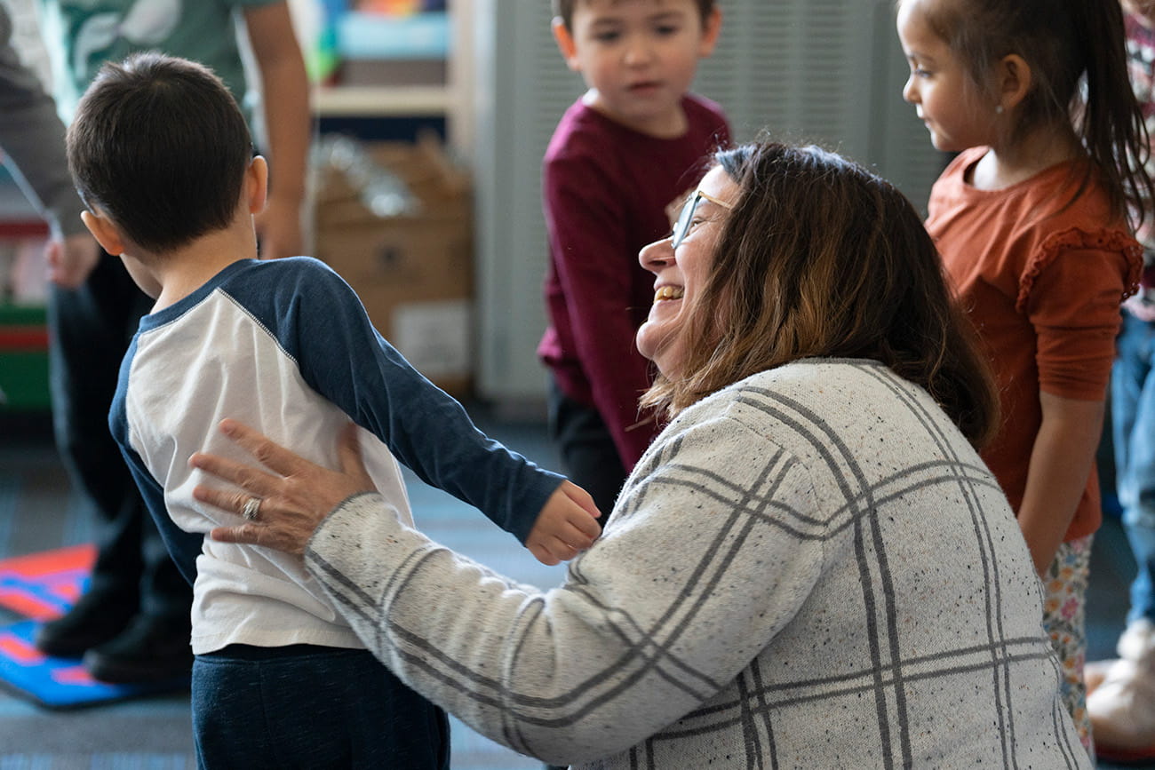 Close up of a teacher smiling at a preschool student in a classroom setting
